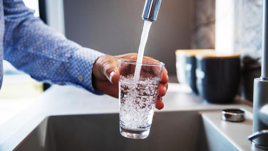 Man in blue dress shirt fills glass with tap water
