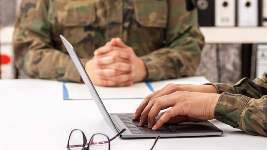 Military officers meet to discuss recruitment. They are using a laptop.