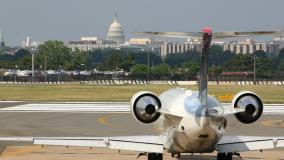 Airplane landing on a runway with Washington, DC skyline, including White House, in background