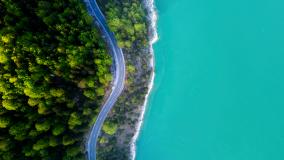 Aerial view from left to right of a forest, a road and bright blue water