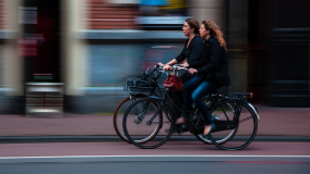 Two women riding bikes on a blurred street