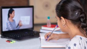 Girl writing with pencil taking instruction from tutor on screen