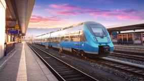 Stock image of a blue passenger train on tracks with pink and purple sunset