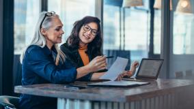 Two women analyzing documents while sitting on a table in office. Woman executives at work in office discussing some paperwork.