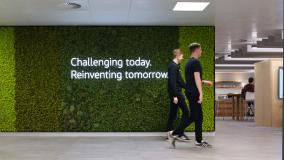 Two men walking past green wall in office area