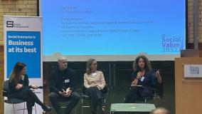 Four people in a panel discussion seated on a stage in front of a screen.