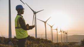 Silhouette of young male engineer holding laptop computer planning and working for the energy industry and standing beside a wind turbines farm power station at sunset time. XXXL size taken with Canon 5D MIV