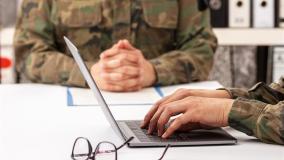 Military officers meet to discuss recruitment. They are using a laptop.