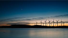 Twilight landscape with wind turbines silhouetted against a colorful sky and reflected in calm water