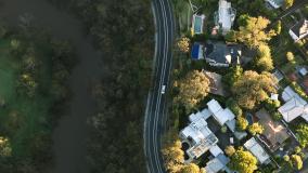 Aerial view of a suburban neighbourhood bordered by a forest, with a winding road separating homes from dense greenery