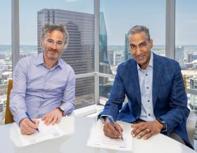 Alex Karp and Bob Pragada signing documents with Dallas skyline in windows behind them