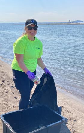 Woman in neon tshirt and purple gloves picking up trash on a beach