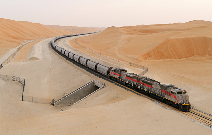 Etihad Rail - train coming round the bend between orange sand dunes