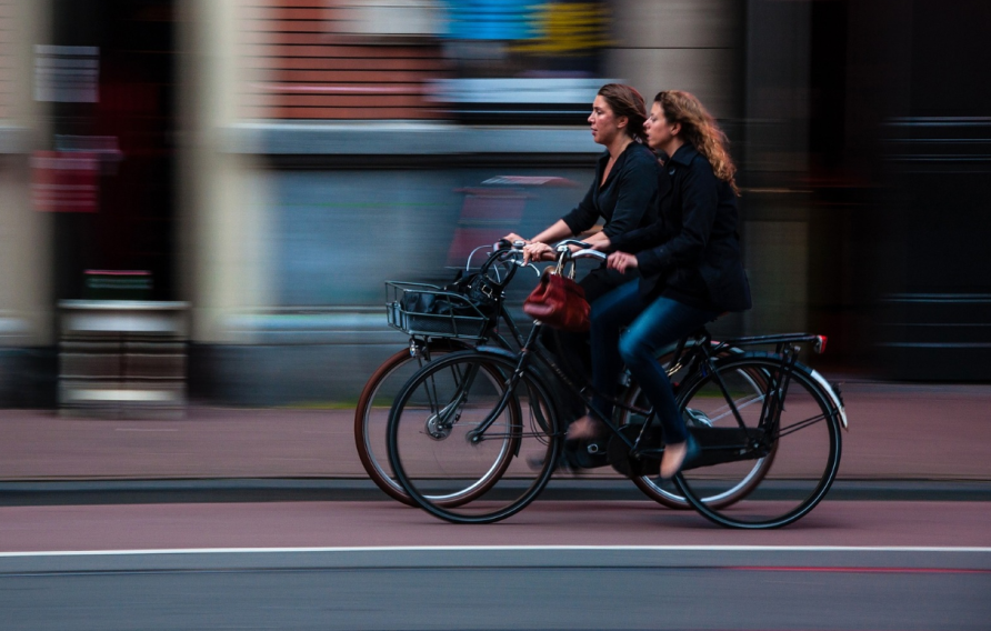 Two women riding bikes on a blurred street