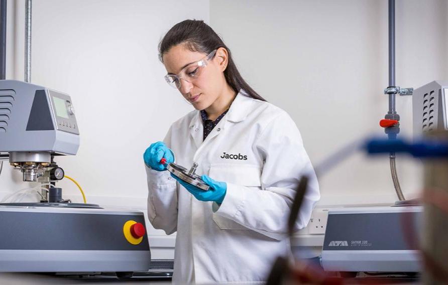 Dark haired woman in a white Jacobs lab coat working with lab equipment