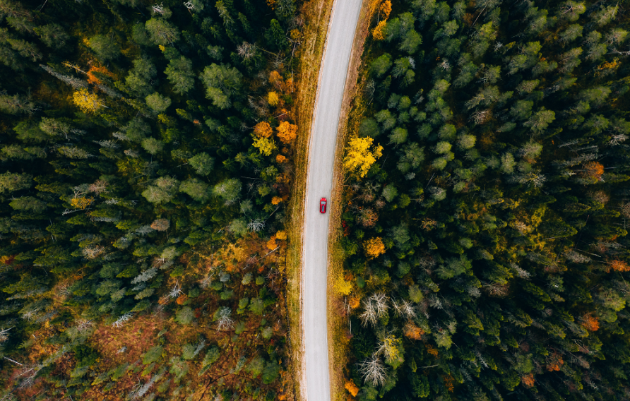 Red car traveling through colorful fall foliage