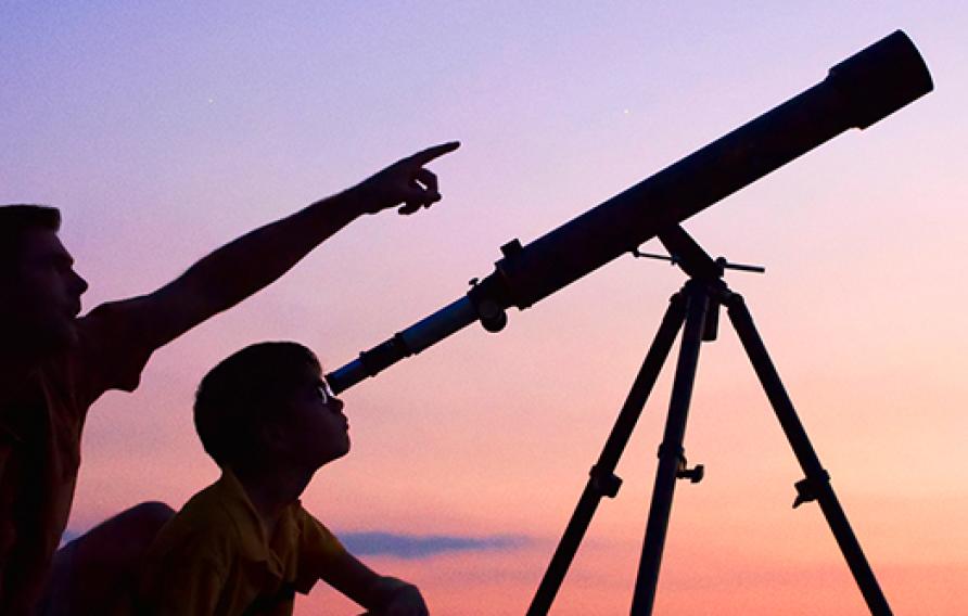 Man and son looking through telescope at dusk