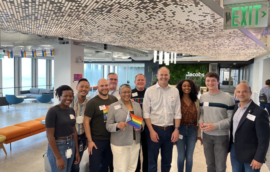 Group of diverse colleagues in an office pose for a picture with a pride flag
