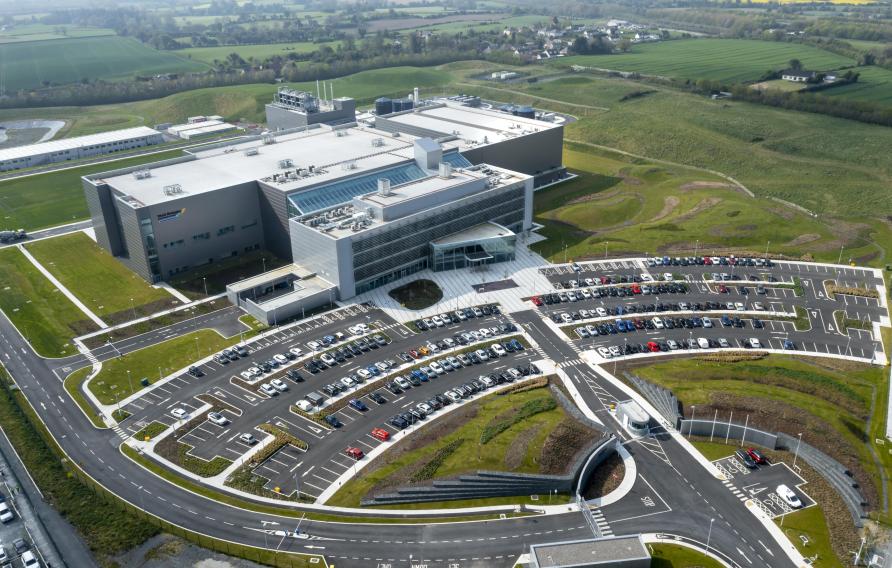 Aerial image of a white office building and parking lot surrounded by green hills