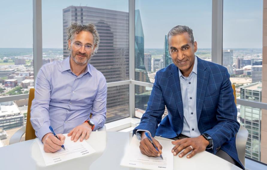 Alex Karp and Bob Pragada signing documents with Dallas skyline in windows behind them