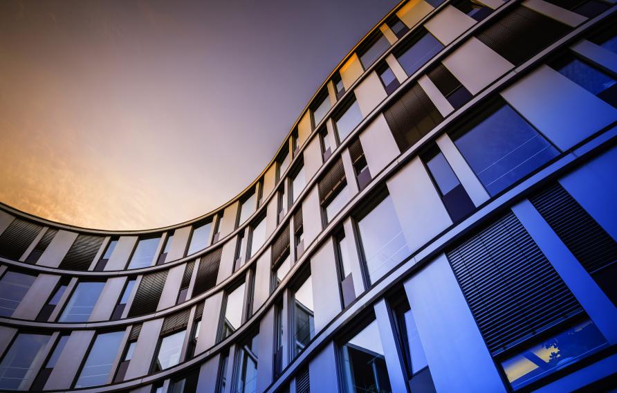 Curved office building with many windoes shaded in multi-colored sky