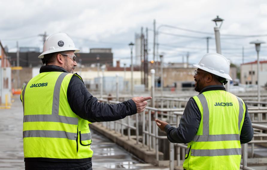 Two men in yellow PPE vests and white hard hats at at treatment facility