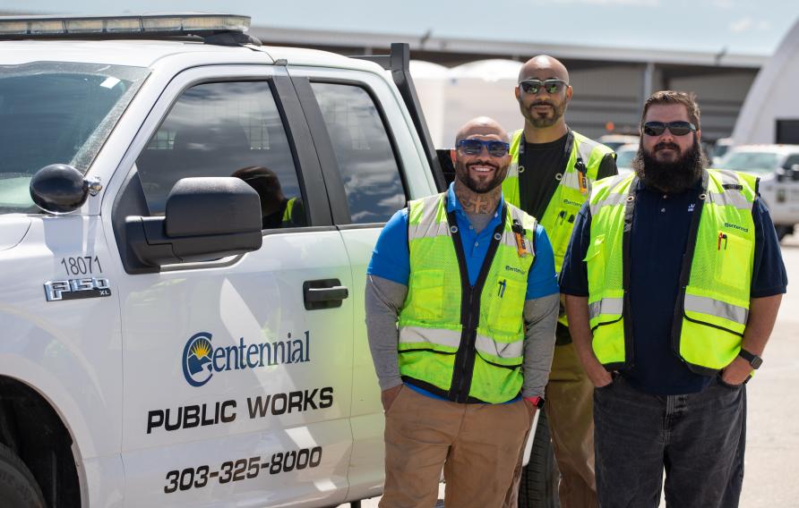 Three men in yellow PPE vests pose in front of white Centennial Public Works pickup truck
