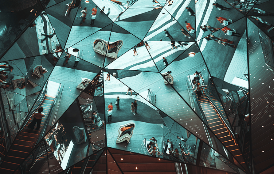 Abstract mirrored ceiling reflecting escalators, stairs, and people in a kaleidoscopic pattern