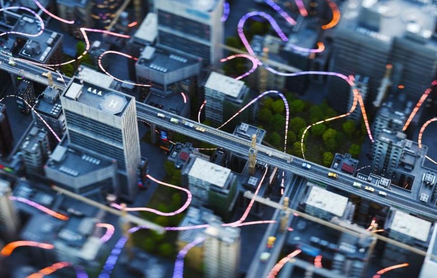 Aerial view of a cityscape with high-rise buildings and colorful light trails to suggest digital connectivity