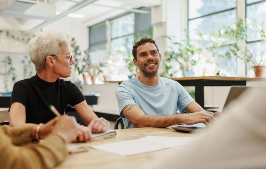 Group of people in a modern office having a meeting around a table with papers and a laptop