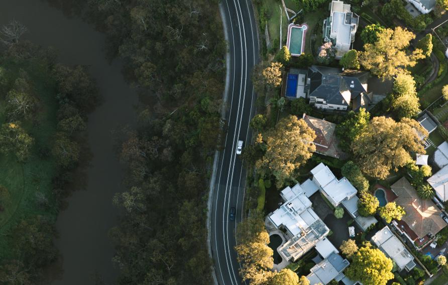 Aerial view of a suburban neighbourhood bordered by a forest, with a winding road separating homes from dense greenery