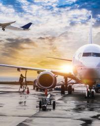 Stock image of an airplane loading with another plane taking off into the sunset 