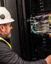 Bearded man in white hard hat and yellow PPE vest looks at a data system