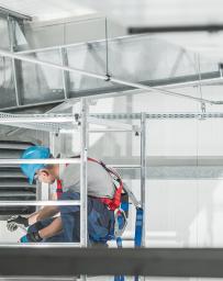 Man in blue hard hat climbs to repair a vent system