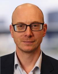 Man wearing glasses with light shirt and plain dark jacket.