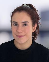 Headshot of woman in black jumper with hair in ponytail.