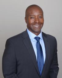 Black man in navy suit with blue tie and light blue dress shirt