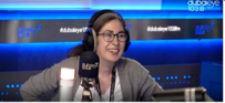Woman in a grey sweater and headphones sits in a blue recording studio