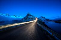 Olstind, a mountain in the Lofoten Islands, Norway, with a car visible and light trails on a road