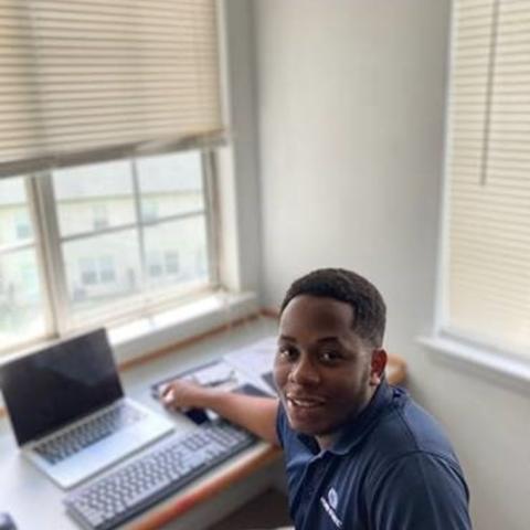 Intern looking over shoulder away from laptop at camera 