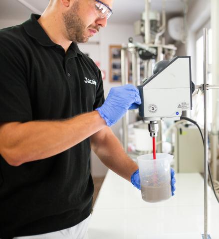 Man in a lab with safety goggles and gloves in a black Jacobs polo