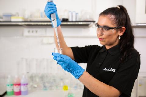Woman with a test tube in a lab in a black Jacobs polo