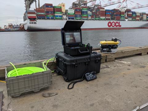 Remotely operated vehicle operates underwater in front of a port and container ship