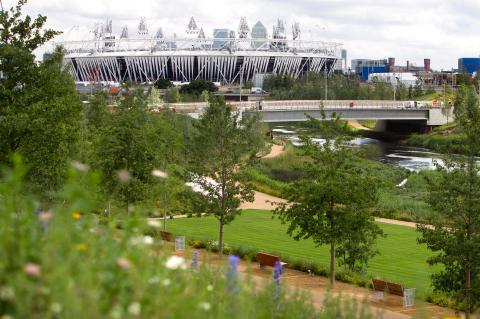 Green trees and parkland with view of the London Olympic Stadium in the distance