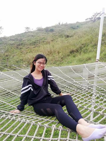 Dark haired Asian woman sits on a webbed hammock