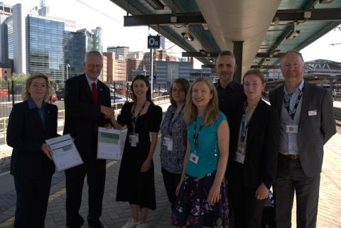 Group of men and women in business attire standing on railway station platform, with two people holding certificates.