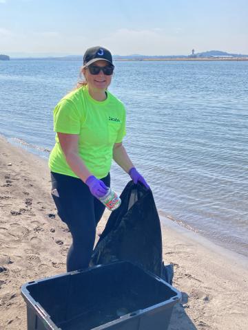 Woman in neon tshirt and purple gloves picking up trash on a beach