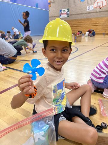 Young hispanic boy with yellow plastic hard hat holds up a blue plastic propeller
