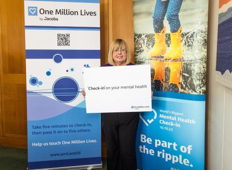 Woman with blond hair holding a banner in front of pop up banners about One Million Lives