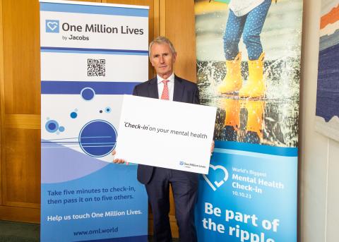 Man in blue suit holding banner in front of pop up banners about One Million Lives